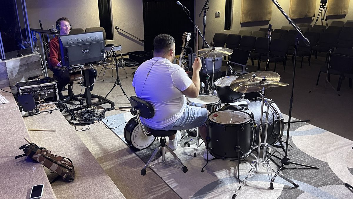 A worship stage with drum mics and a tech at a monitor before a service